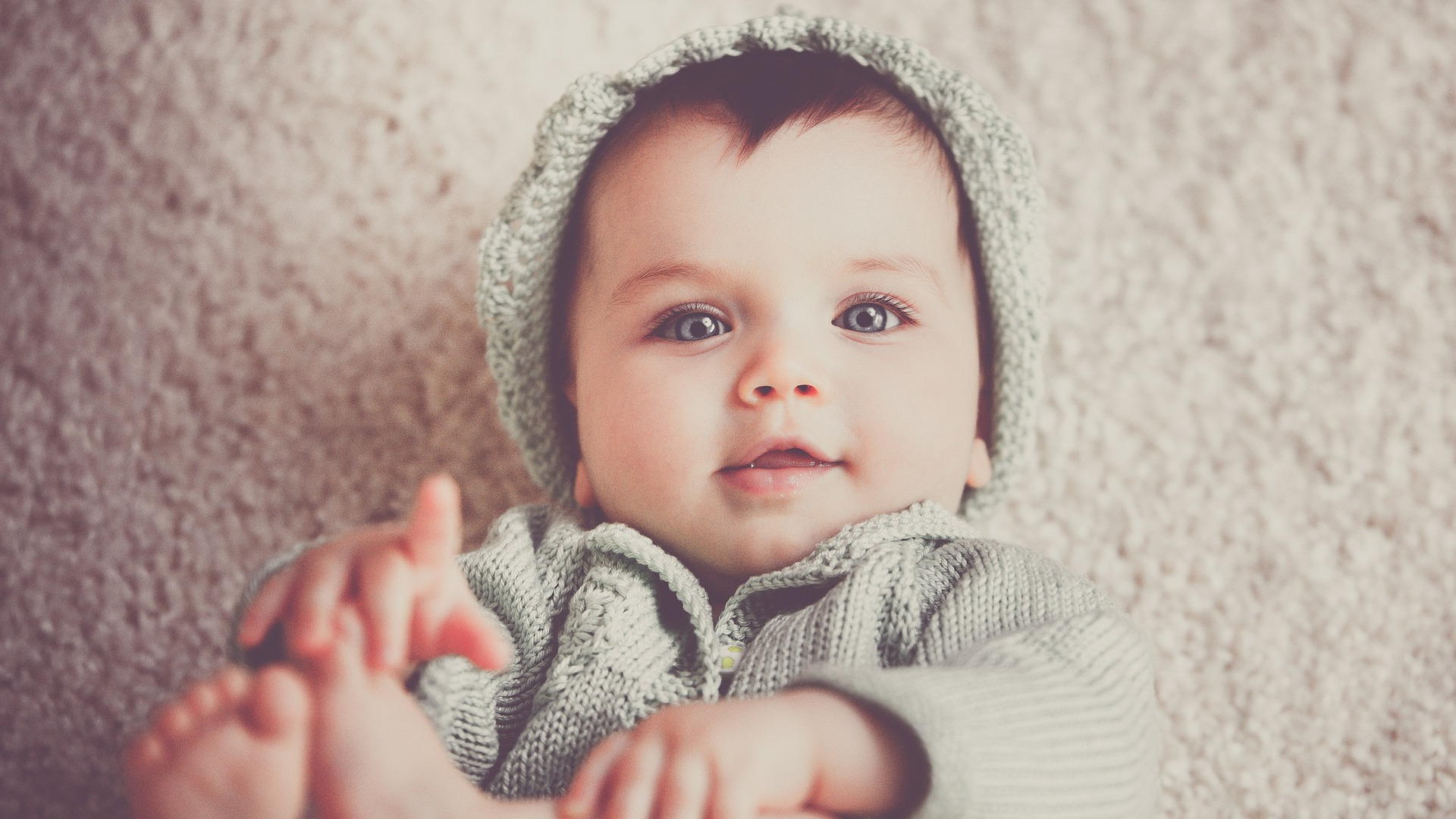 Happy infant laying on the ground holding their feet.